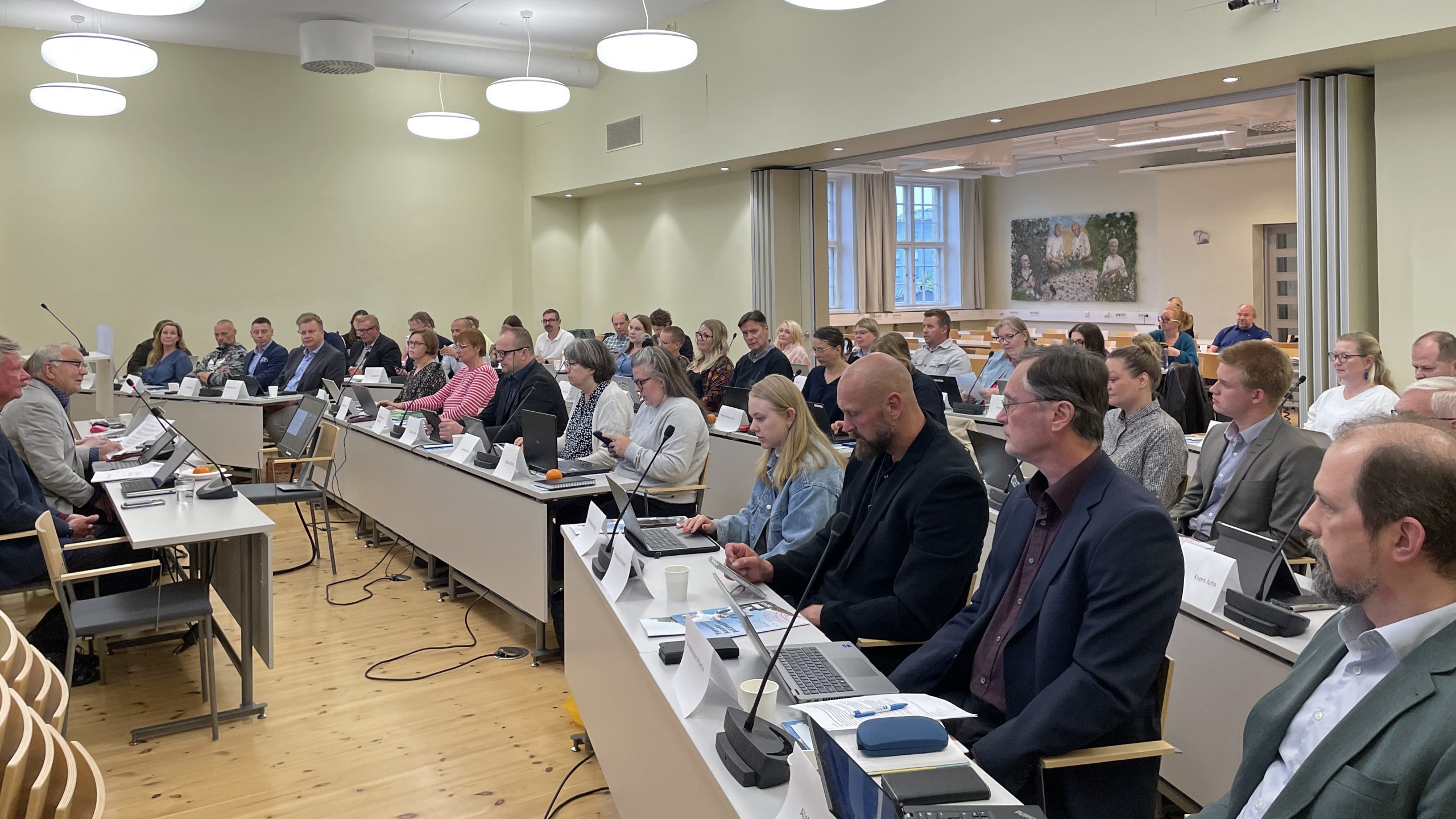 Useita ihmisiä istuu isossa kokoustilassa riveissä. Valtuusto kokoontuu.