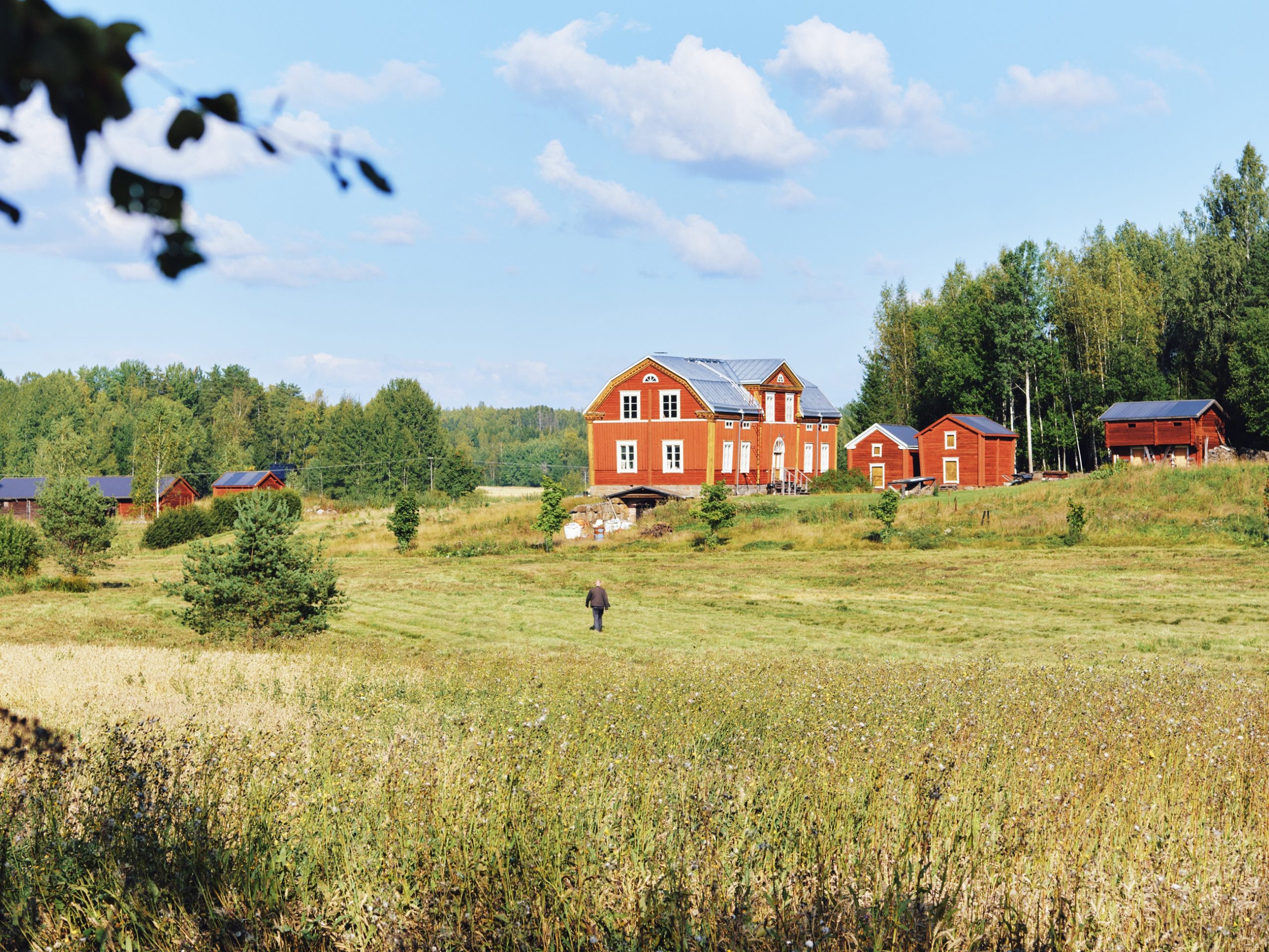 Gammalt timmerhus med gårdsbyggnad på backen bakom åkern.